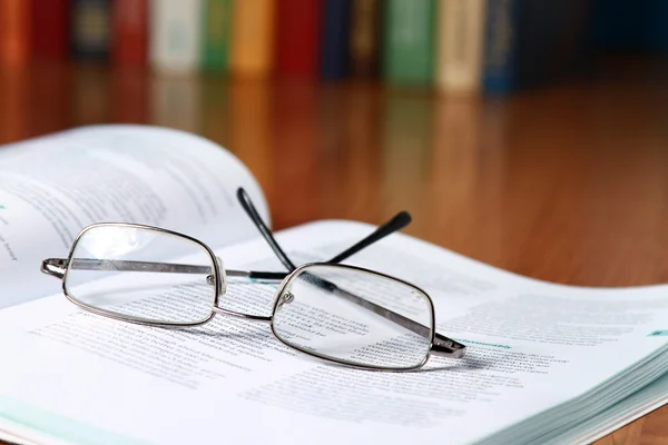 En öppen bok med glasögon mot böcker — Stockfoto
