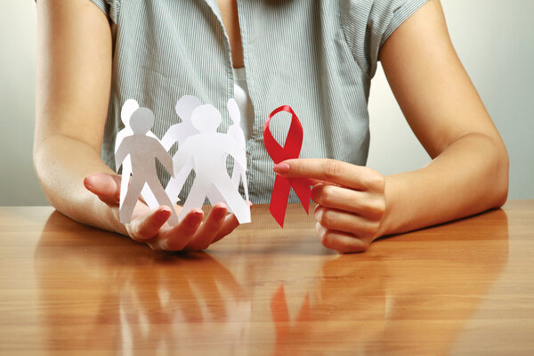 A woman holding paper peolple and an aids red ribbon