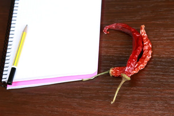 Peppers near a notebook and a pencil — Stock Photo, Image