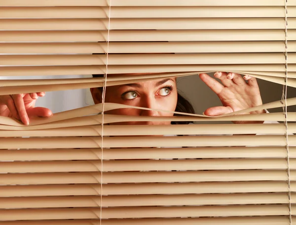 Mulher olhando através de persianas — Fotografia de Stock
