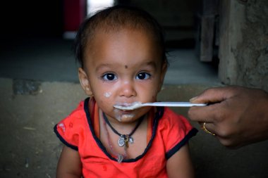 Hintli kırsal anne, 10 aylık bebeğini kaşıkla besliyor, çocuk için ilk katı yiyecek, seçici odaklanma.