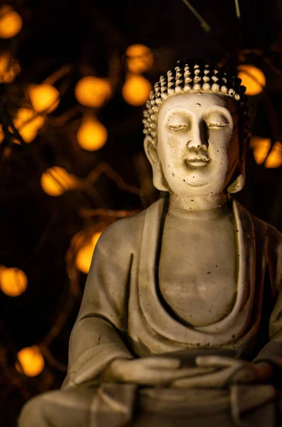 Buddha statue at night with lights. Figure with hands together in prayer mode. The focus is on the face.