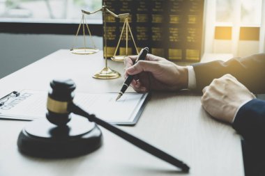 Avukatın eli kalem tutuyor ve ofiste hukuki danışmanlık hizmeti veriyor. Adalet terazisi ve tokmak çekiciyle..