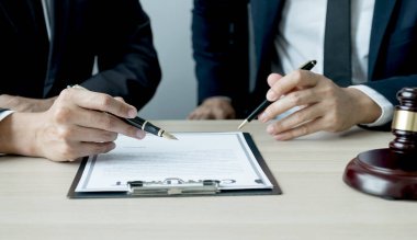 Avukatın eli kalem tutuyor ve ofisteki adama hukuki danışmanlık hizmeti veriyor. Adalet terazisi ve tokmak çekiciyle..