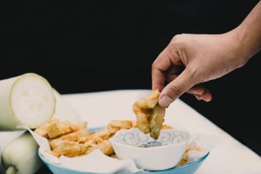 Hand picked fried calabash and dipped in seafood sauce on a black background.