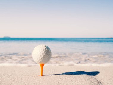 The golf ball is on the tee, embroidered on the sand beach with the sea in the background.