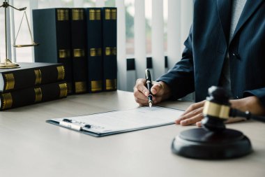 Kadın avukat elinde adalet terazisi ve tokmak çekiciyle büroda oturuyor. Müşterilere tavsiye vermek için iş anlaşmazlıklarında hukuk okuyun.