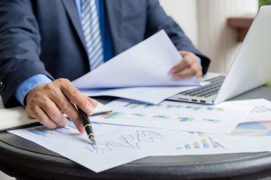 İş adamı kalemini tutuyor, iş hedeflerini belirlemek ve yeni hedefe ulaşmayı planlamak için merkez ofisteki bilgisayarla grafiği analiz ediyor..