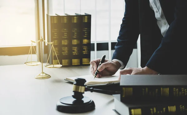 Lawyer hand holding pen and providing legal consult business dispute service at the office with justice scale and gavel hammer.