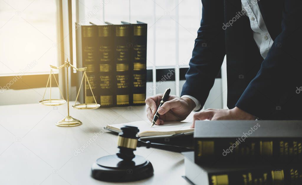 Lawyer hand holding pen and providing legal consult business dispute service at the office with justice scale and gavel hammer.