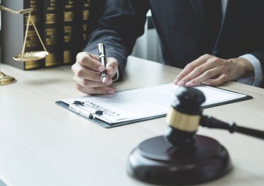 Avukatın eli kalem tutuyor ve ofisteki adama hukuki danışmanlık hizmeti veriyor. Adalet terazisi ve tokmak çekiciyle..