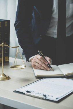 Avukatın eli kalem tutuyor ve ofiste hukuki danışmanlık hizmeti veriyor. Adalet terazisi ve tokmak çekiciyle..