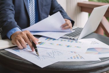 İş adamı kalemini tutuyor, iş hedeflerini belirlemek ve yeni hedefe ulaşmayı planlamak için merkez ofisteki bilgisayarla grafiği analiz ediyor..