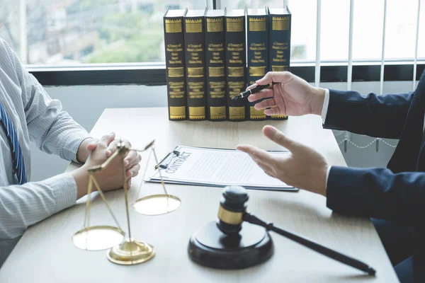 Lawyer hand holding pen and providing legal consult business dispute service to the man at the office with justice scale and gavel hammer.