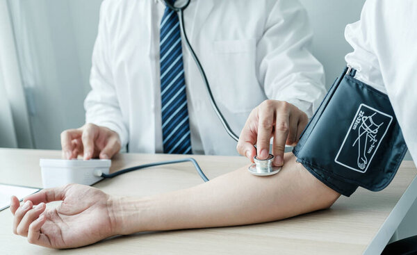 Doctor evaluates the patient with a stethoscope, blood pressure monitor and records the results, health medical checkup concept.