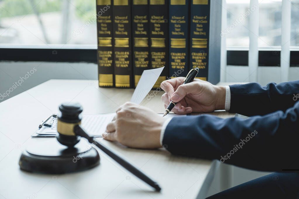 Lawyer hand holding pen and providing legal consult business dispute service at the office with justice scale and gavel hammer.