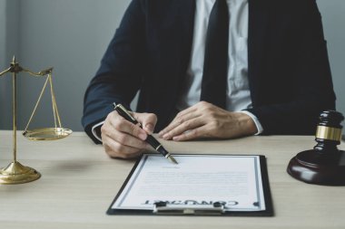Avukatın eli kalem tutuyor ve ofiste hukuki danışmanlık hizmeti veriyor. Adalet terazisi ve tokmak çekiciyle..