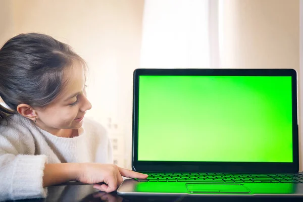 Ein junges Mädchen blickt auf den grünen Bildschirm eines Laptops und drückt mit dem Finger auf die Tasten. — Stockfoto