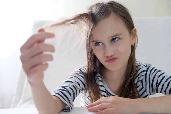 Kudłaty nastolatka patrząc na jej włosy trzymając kosmyk włosów w jej rękach — Zdjęcie stockowe