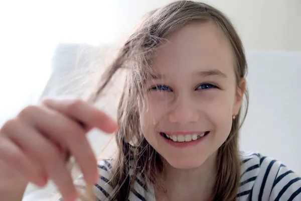 Uśmiechnięta dziewczyna trzyma splątane włosy w dłoni — Zdjęcie stockowe