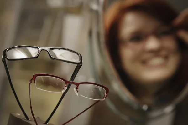 Affichage de fenêtre d'opticien avec la femme essayant des lunettes dans le miroir en arrière-plan — Photo