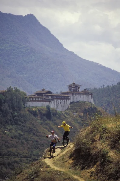 Unicyclists Riding On Path With Old Building In Background — Stock Photo, Image