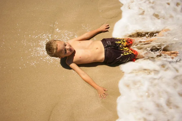 Menino deitado na praia na água — Fotografia de Stock