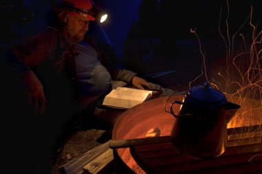 Man Reading Bible At Night Next To Fire clipart