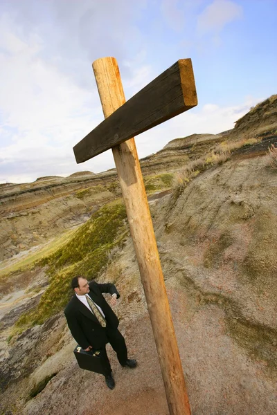 Бизнесмен смотрит на часы, стоящие на кресте — стоковое фото