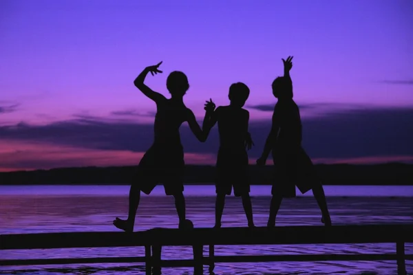 Три силуэта мальчиков на причале против заката — стоковое фото
