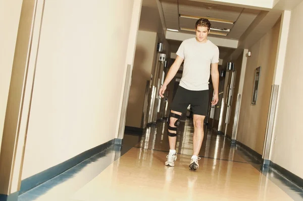 Ein junger Mann, der mit einer Kniestrebe in einem Krankenhaus geht — Stockfoto