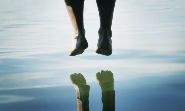 Un par de pies colgando sobre el agua — Foto de Stock