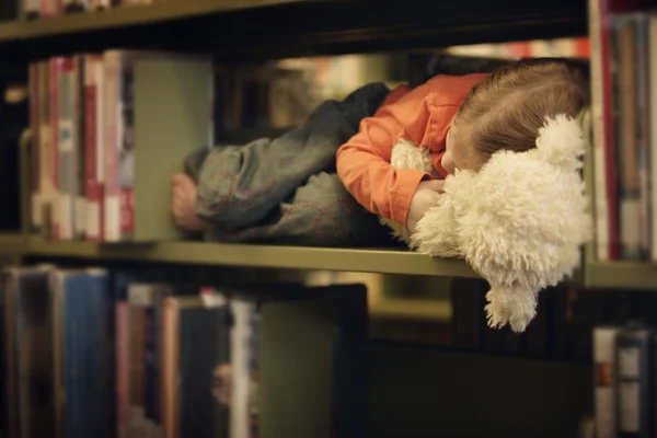 Niño cae dormido en un estante de libros —  Fotos de Stock