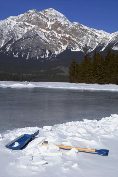 Snöskyffel av en frusen sjö mot bergen — Stockfoto