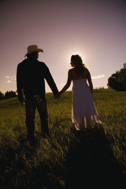 Man And Woman Walking Hand-In-Hand In Field In Sunset clipart