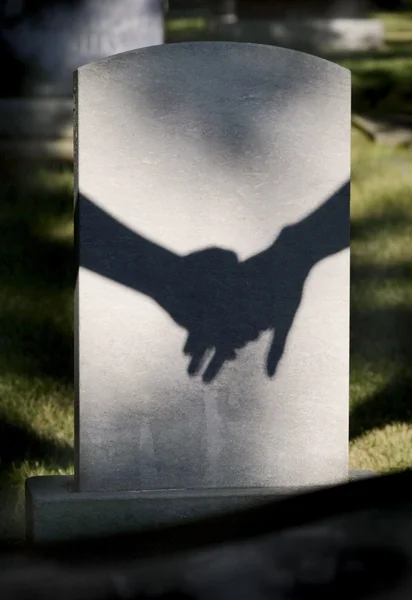 影子在墓碑上的两个着紧握的手 — 图库照片