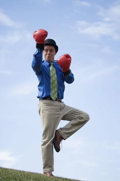 Человек в боксёрских перчатках и шапке дерби стоит на одной ноге — стоковое фото