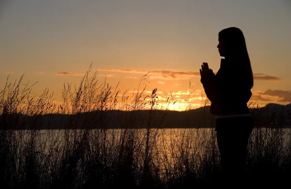 Una ragazza adolescente prega al tramonto vicino all'oceano . — Foto Stock