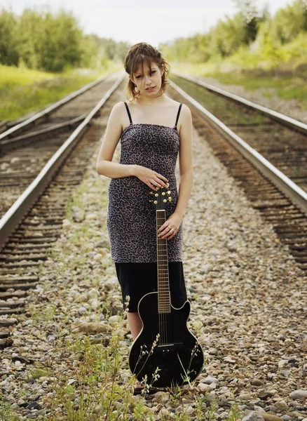 Jeune femme tenant la guitare acoustique sur les rails de train — Photo