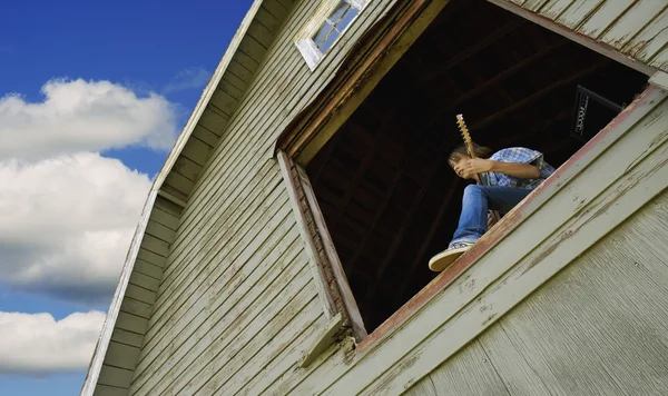 Chlapec, hrál na kytaru v stodola okna — Stock fotografie