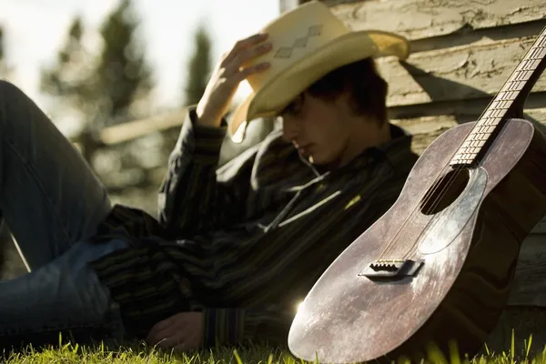 Giovane uomo che indossa Cowboy cappello dormire contro esterno di costruzione con chitarra — Foto Stock