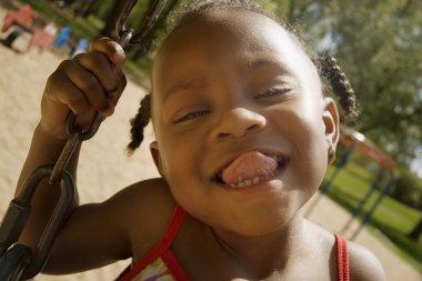Young Girl Sticking Out Her Tongue While On The Swingset In The Park clipart
