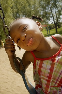 Young Girl Sticking Out Her Tongue While On The Swing Set At The Park clipart