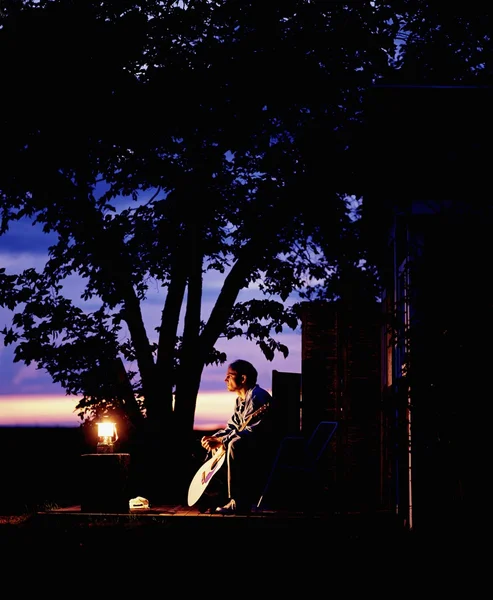 Mężczyzna siedzi z gitara latarnia o zmierzchu — Zdjęcie stockowe