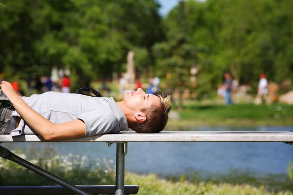 Homem deitado em um banco perto de uma lagoa — Fotografia de Stock