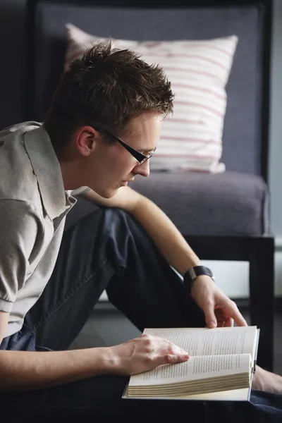 Junger Mann sitzt auf dem Boden und liest ein Buch — Stockfoto