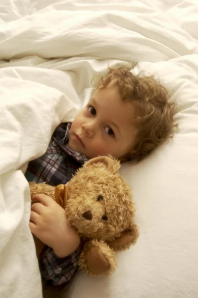 Мальчик лежит в постели с плюшевым мишкой — стоковое фото