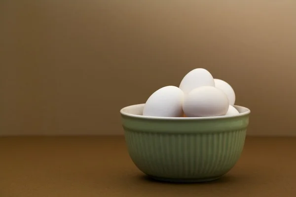 Huevos blancos en tazón verde sobre mesa marrón —  Fotos de Stock