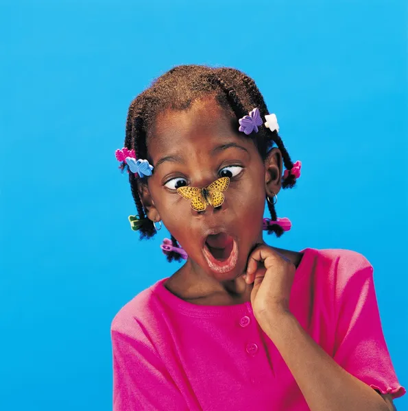 Africano bambina con farfalla barrette e un farfalla su il suo naso guardando sorpreso — Foto Stock