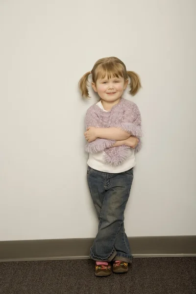 Leende liten flicka lutad mot en vägg med armarna korsade — Stockfoto